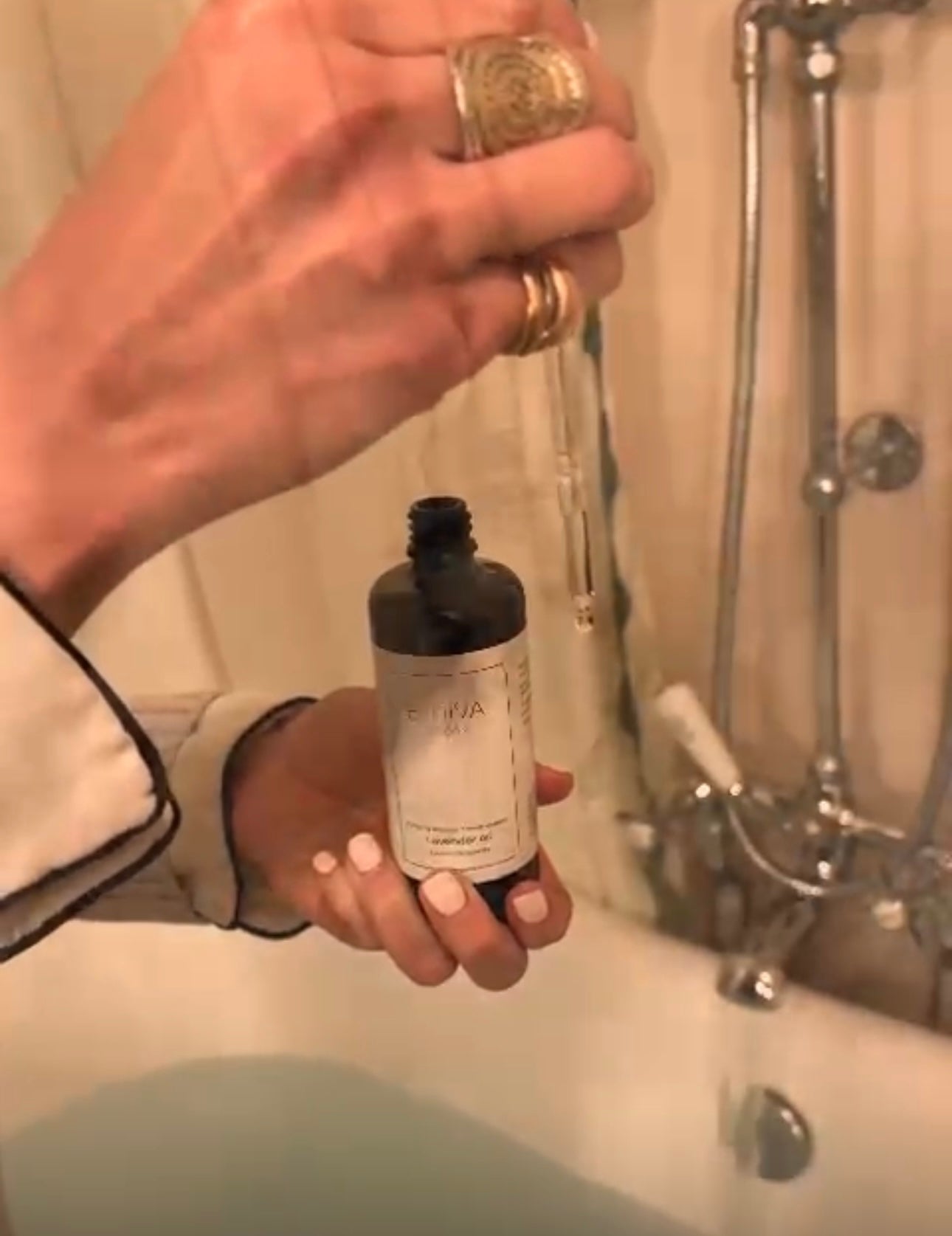 Bath with water running and woman releasing drops of lavender oil from a pipette dropper