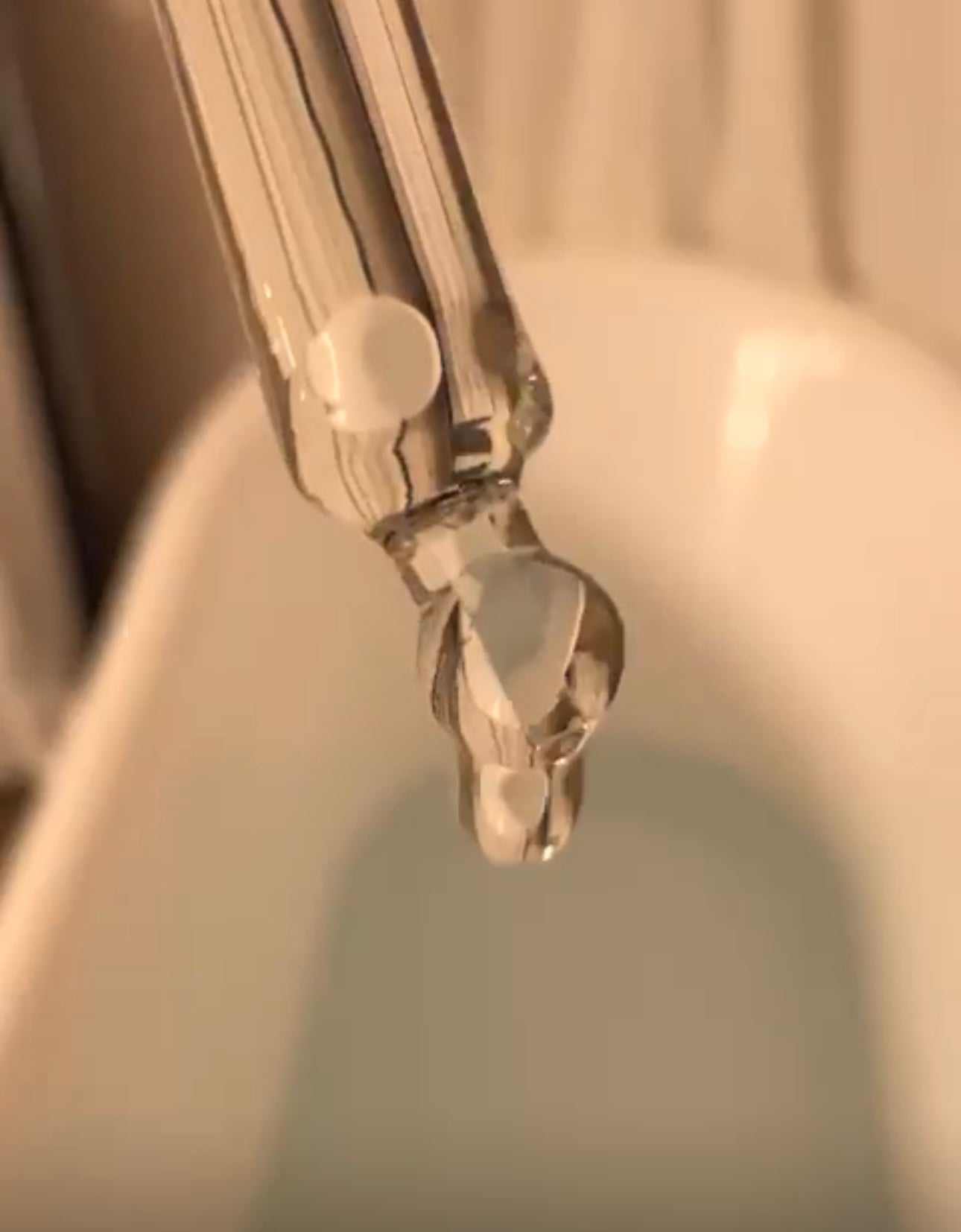 Pipette dropper being held over bath with running water, releasing carefully measured drops of lavender oil into the bath