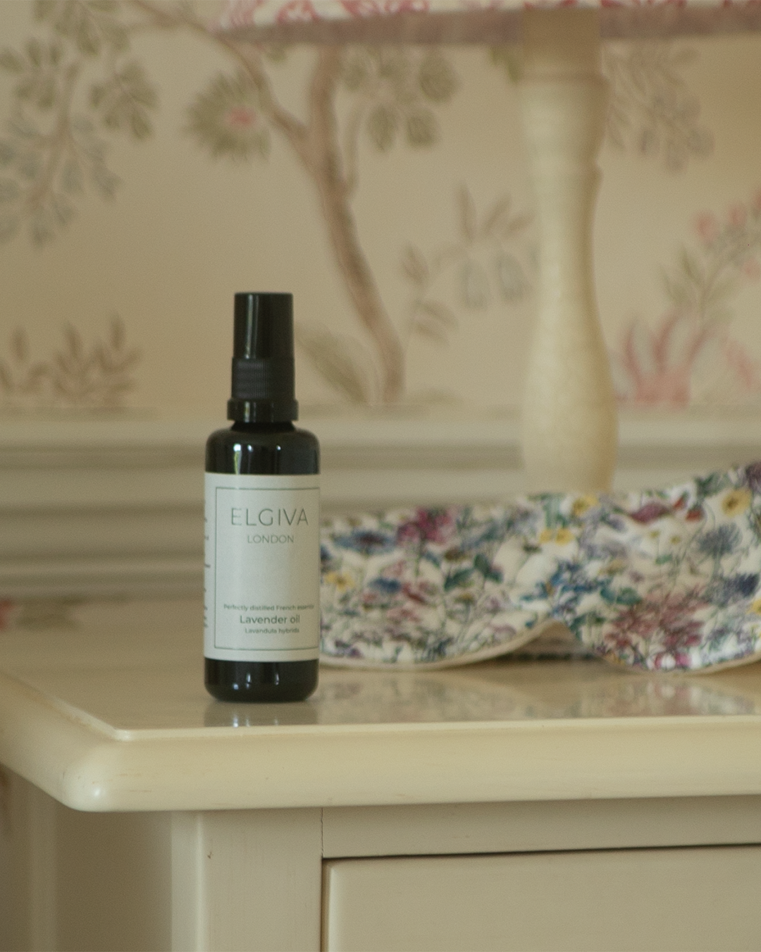 Elgiva London 50ml lavender oil bottle styled on a bedside table with a sleep eye mask, vertical crop